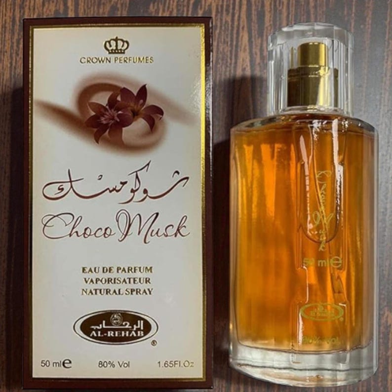 Puede incluir: Un juego de botella y caja de perfume. La caja es crema y marr&oacute;n con el texto "Choco Musk" y "Crown Perfumes". El frasco de perfume es transparente con una tapa dorada y contiene un l&iacute;quido dorado. La botella es de 50 ml y 1,65 fl oz.