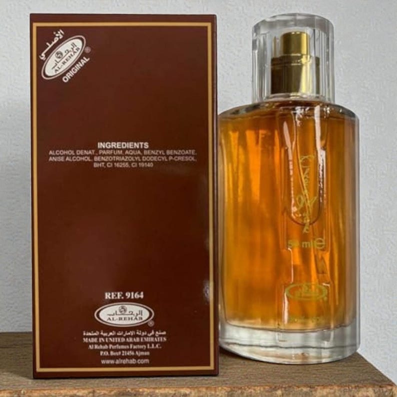 Puede incluir: Un juego de botella y caja de perfume. La botella es transparente con un l&iacute;quido dorado en su interior. La caja es marr&oacute;n con texto blanco y escritura &aacute;rabe. El texto de la caja incluye los ingredientes y la marca, Al-Rehab.
