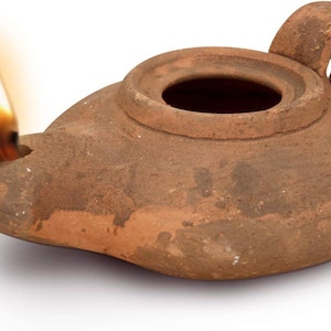 May include: A terracotta oil lamp with a lit flame. The lamp has a rounded body, a spout, and a handle. The flame is yellow and orange, and the lamp appears to be ancient or antique.