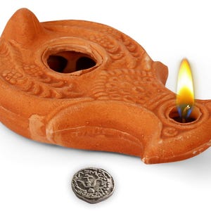 May include: A terracotta oil lamp with a burning flame. The lamp is a warm orange colour and has a detailed design. A small, silver coin is below the lamp. The flame is yellow and orange.