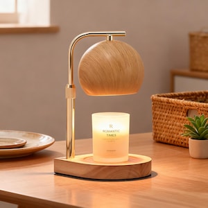 May include: A candle warmer with a wooden shade and base, and a gold-colored metal arm. The candle warmer has a lit candle inside with the text "ROMANTIC TIMES". The candle warmer is on a wooden table.