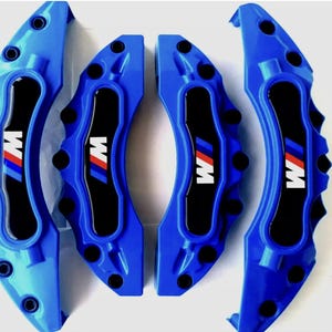 Puede incluir: Juego de cuatro pinzas de freno azul brillante con detalles en negro. Cada pinza muestra el logotipo "M" blanco, azul y rojo. Estas pinzas de automoción se presentan sobre un fondo blanco.