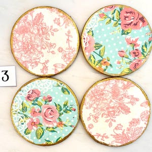 May include: Four round coasters with floral designs. Each coaster has a gold painted edge. The patterns include pink roses, floral toile, and a blue background with white polka dots. The number "3" is in the image.