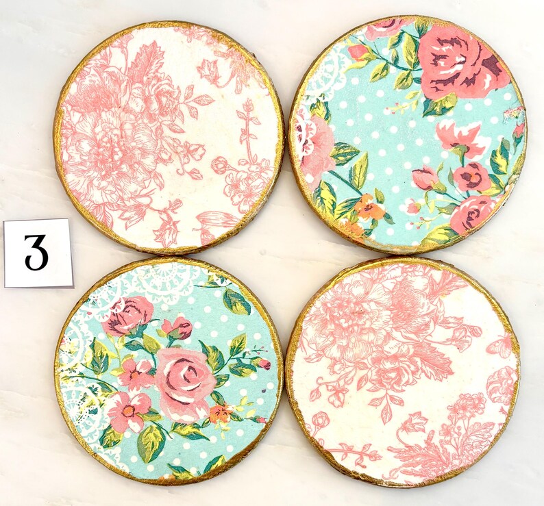 May include: Four round coasters with floral designs. Each coaster has a gold painted edge. The patterns include pink roses, floral toile, and a blue background with white polka dots. The number "3" is in the image.