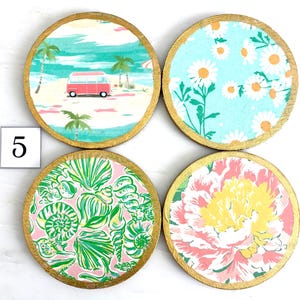 K&ouml;nnte beinhalten: Set aus vier runden Untersetzern mit goldfarbenen R&auml;ndern. Jeder Untersetzer hat ein anderes Design: eine Strandszene mit einem roten Van, wei&szlig;e G&auml;nsebl&uuml;mchen auf blauem Grund, Muscheln auf rosa und ein rosa-gelbes Blumenmuster.