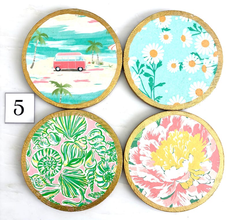 K&ouml;nnte beinhalten: Set aus vier runden Untersetzern mit goldfarbenen R&auml;ndern. Jeder Untersetzer hat ein anderes Design: eine Strandszene mit einem roten Van, wei&szlig;e G&auml;nsebl&uuml;mchen auf blauem Grund, Muscheln auf rosa und ein rosa-gelbes Blumenmuster.