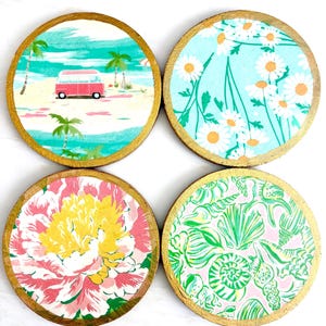 K&ouml;nnte beinhalten: Vier runde Untersetzer aus Holz mit goldfarbenen R&auml;ndern. Jedes Set hat ein anderes Design: eine Strandszene mit einem roten Van, wei&szlig;e G&auml;nsebl&uuml;mchen auf blauem Grund, eine gro&szlig;e rosa und gelbe Blume und ein gr&uuml;n-rosa Muschelmuster.