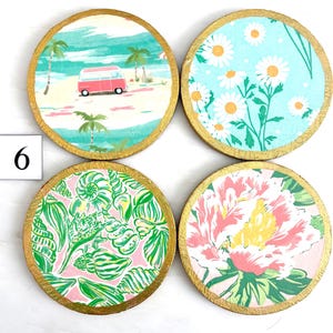 K&ouml;nnte beinhalten: Vier runde Untersetzer-Set mit goldfarbenen R&auml;ndern. Jedes Set zeigt ein anderes Design: eine Strandszene mit einem rosa Van, wei&szlig;e G&auml;nsebl&uuml;mchen auf blauem Grund, Muscheln auf rosa und ein Blumenmuster.