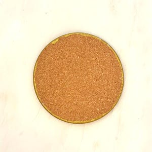 K&ouml;nnte beinhalten: Ein runder Untersetzer aus Kork mit goldfarbenem Rand. Der Untersetzer besteht aus nat&uuml;rlichem Korkmaterial und soll Oberfl&auml;chen vor Hitze und Feuchtigkeit sch&uuml;tzen. Der Untersetzer hat einen Durchmesser von etwa 10 cm.