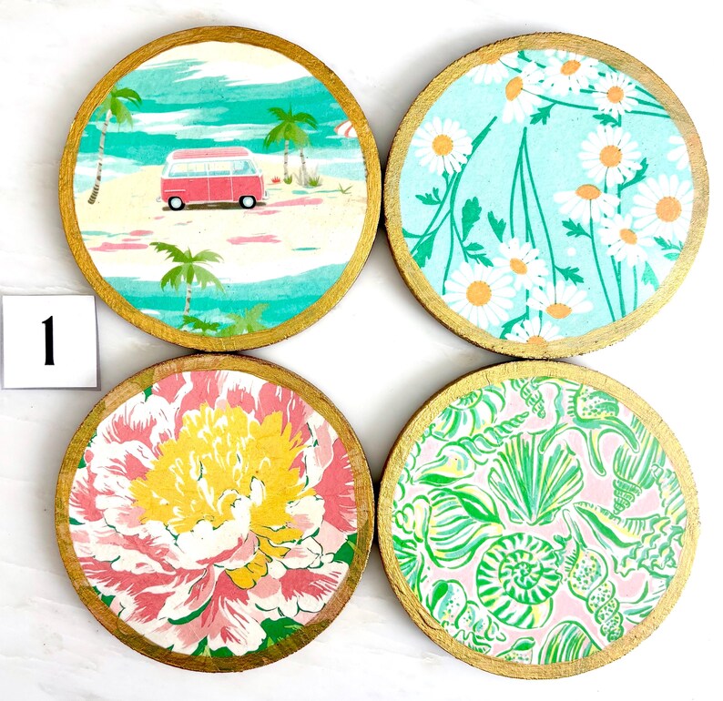 K&ouml;nnte beinhalten: Set aus vier runden Untersetzern mit goldenen R&auml;ndern. Jedes Set zeigt ein anderes Design: eine Strandszene mit einem roten Van, wei&szlig;e G&auml;nsebl&uuml;mchen auf blauem Hintergrund, ein rosa-gelbes Blumenmuster und ein gr&uuml;nes Muschelmuster.