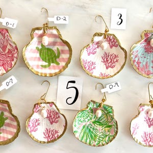 May include: Eight decorative scallop shells with gold-painted edges, each featuring a unique pattern including sea turtles, coral, and floral designs. Each shell has a gold hook and a white pearl bead attached. Labels D-1, D-2, D-4, D-7, D-9, 3, 5, and 6 are visible.