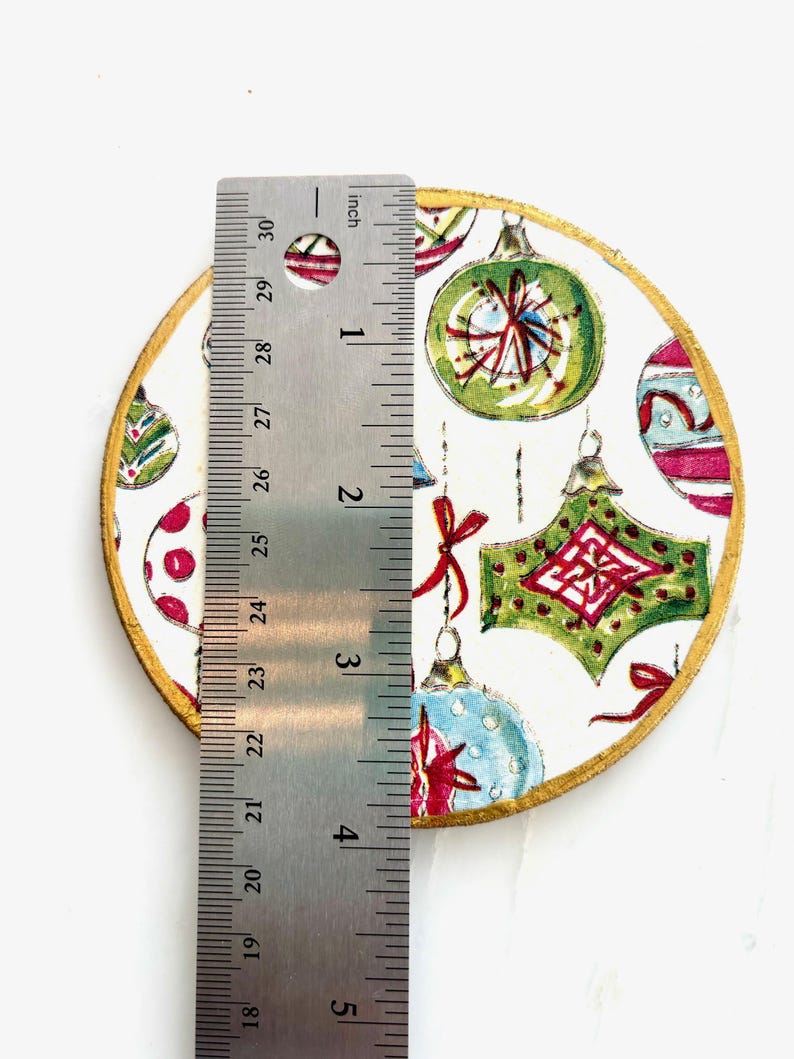 May include: A round, decorative Christmas ornament with a gold edge. The ornament features a white background with colorful, hand-painted Christmas ornament designs. The ornament is approximately 4 inches in diameter.