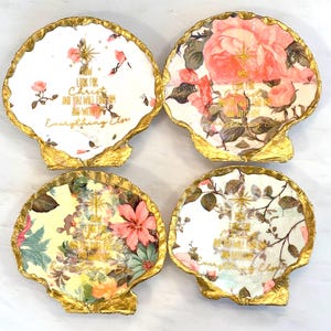 May include: Four decorative seashell-shaped coasters with gold trim. Each coaster features a floral design with text in gold. The floral patterns include pink roses, and other colorful flowers. The text on each coaster reads "Look for Christ and you will find everything else."
