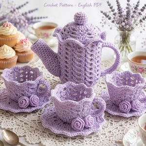 Può includere: Uno schema all'uncinetto per un servizio da tè con un copriteiera color lavanda e tre tazze abbinate con piattini, ciascuna decorata con piccole rose all'uncinetto. Il set include una teiera con coperchio e tazze con bordi smerlati, tutto in filato viola chiaro. Il testo Crochet Pattern - English PDF è visibile in alto.