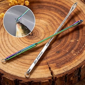 May include: Two fishing needle tools with a rainbow finish and the text "Best Fisherman" engraved on the handles. One is silver, the other has a rainbow finish. A close-up shows a fish being caught with the tool.