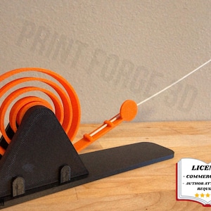 May include: A 3D-printed kinetic sculpture featuring a black base and a triangular support structure. Orange spiral rings and a rod with an orange tip extend from the base. The sculpture is designed to move.
