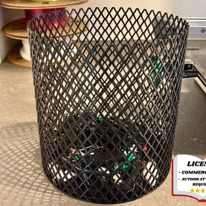 May include: A black metal mesh wastebasket filled with various electronic components. The cylindrical bin has a diamond pattern and sits on a gray surface. The image includes a license notice in the bottom right corner.