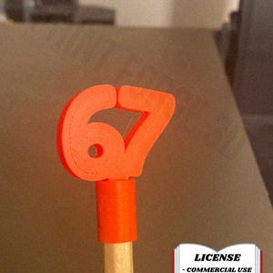 May include: A bright orange number 67, 3D-printed, attached to a pencil. The pencil is held upright. The image includes a license graphic with the text "LICENSE - COMMERCIAL USE - AUTHOR ATTRIBUTION REQUIRED". The @CARTERRA logo is in the bottom left.
