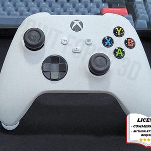 Puede incluir: Un mando Xbox blanco con botones negros y botones de acción de colores. El mando tiene una cruceta, dos joysticks y varios botones de función. La imagen incluye el texto "PRINT FOR 3D" y un aviso de licencia.