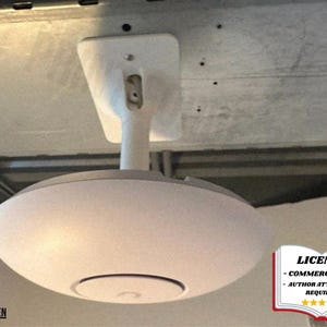 Puede incluir: Un ventilador de techo blanco y gris con una pantalla redondeada que difunde la luz. El ventilador está montado en el techo con un soporte blanco. La imagen incluye un aviso de licencia en la esquina inferior derecha.