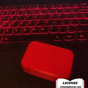 May include: A red rectangular object rests on a laptop keyboard with red backlit keys. The keyboard is black, and the laptop's brand name, LEGION, is visible at the top. A license badge is in the bottom right corner.