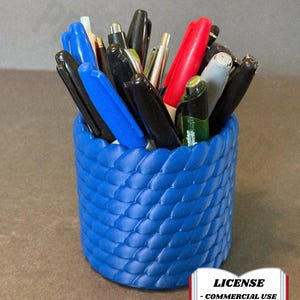 Op de afbeelding: Een blauwe pennenhouder met een geweven textuur, gevuld met verschillende pennen en stiften in zwart, blauw, rood en zilver. De afbeelding bevat de tekst: "LICENSE - COMMERCIAL USE - AUTHOR ATTRIBUTION REQUIRED".