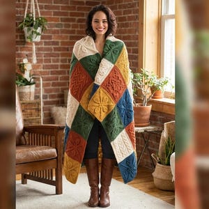Puede incluir: Una persona envuelta en una manta de punto patchwork colorida. La manta presenta cuadrados en crema, naranja, verde, amarillo y azul, con patrones de punto trenzado y floral. La persona lleva botas marrones. El fondo incluye una pared de ladrillo y plantas de interior.