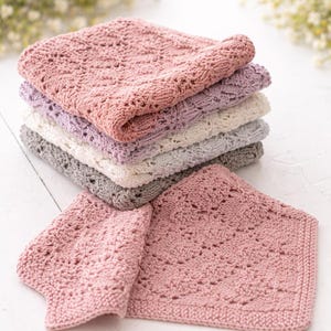 Può includere: Una pila di sei asciugamani di stoffa lavorati a maglia in vari colori pastello: rosa antico, lavanda, crema e grigio. Gli asciugamani hanno un design strutturato e traforato. Un asciugamano è aperto, mostrando il motivo.