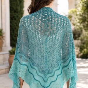 Puede incluir: Un chal triangular con un intrincado patrón de encaje calado en tonos azul verdoso y turquesa. La prenda presenta una transición de color degradada con un diseño de borde ondulado distintivo a lo largo del dobladillo, hecho de hilo fino.