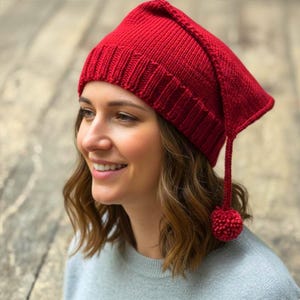 Puede incluir: Un gorro rojo tejido con una punta larga y puntiaguda y un pequeño pompón. El gorro está hecho de un hilo grueso y texturizado. El gorro es de un tono rojo vibrante y está diseñado para ser usado en la cabeza.