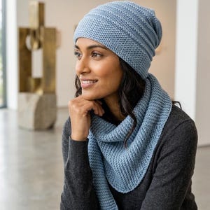 Puede incluir: Un conjunto de gorro y bufanda de punto azul claro. El gorro es de estilo gorro con canalé horizontal. La bufanda tiene forma triangular, también con textura acanalada. El conjunto está hecho de un material suave, posiblemente lana.