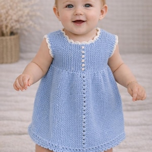 Puede incluir: Vestido de bebé de punto azul claro con un ribete blanco festoneado alrededor del cuello y las sisas. El vestido presenta una fila de botones en la parte delantera y una falda acampanada. El bebé sonríe y está de pie.
