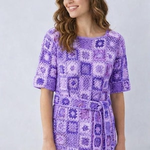 Puede incluir: Top de crochet morado de manga corta con cinturón a juego. La parte superior presenta un diseño de patrón cuadrado en varios tonos de morado. La modelo sostiene un sombrero de paja y una bolsa tejida.