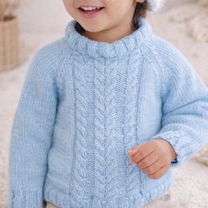 Puede incluir: Un suéter de punto trenzado azul claro con cuello alto. El suéter presenta un diseño de trenza central y puños acanalados. La suave y texturizada prenda de punto es adecuada para ropa de niños.