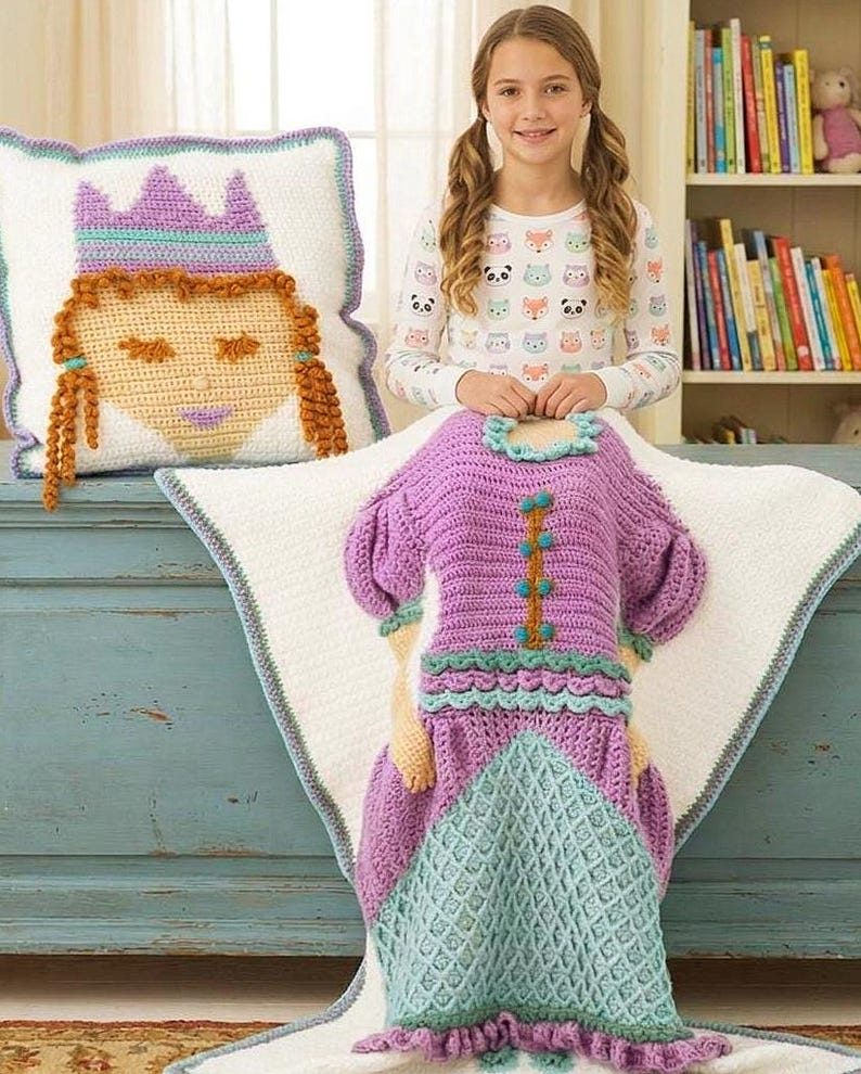 Peut inclure: Ensemble de couverture et d'oreiller sur le th&egrave;me de la princesse au crochet. La couverture est violette et sarcelle, con&ccedil;ue pour ressembler &agrave; une robe. L'oreiller repr&eacute;sente un visage de princesse avec une couronne. L'ensemble est sur fond blanc avec une bordure bleue.