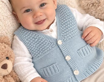 May include: A baby wearing a light blue knitted vest with three white buttons and two front pockets. The baby is also wearing a white collared shirt and beige pants. A teddy bear is visible on the left side of the image.