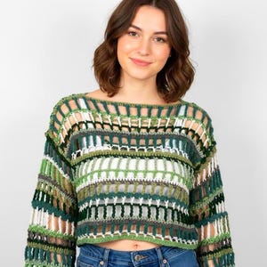 Puede incluir: Un top de ganchillo verde, blanco y gris con mangas largas. El diseño de tejido abierto presenta una mezcla de colores y texturas, creando un look único y elegante. El top es corto y el escote es amplio, de estilo barco.