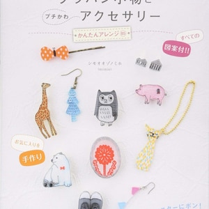 以下が含まれることがあります： 手作りのアクセサリーや小物コレクション。キリン、フクロウ、豚、猫のペンダントなど。画像には、リボンヘアクリップ、イヤリング、靴も含まれています。表紙のテキストは「かわいいアクセサリーとグッズレシピ」と書かれています。
