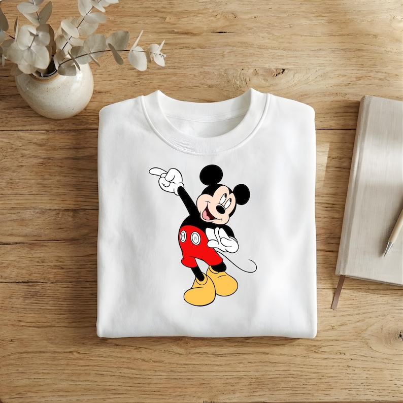 Puede incluir: Sudadera blanca de cuello redondo con un dise&ntilde;o de Mickey Mouse se&ntilde;alando. Mickey lleva pantalones cortos rojos, zapatos amarillos y guantes negros. La sudadera est&aacute; hecha de un material suave.