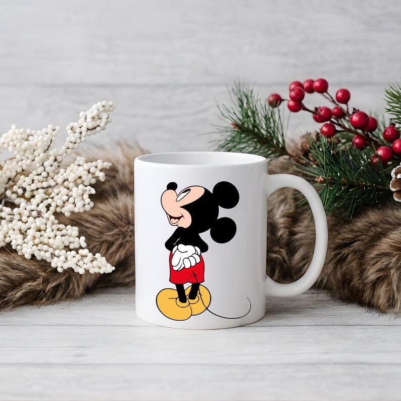 Puede incluir: Taza de cer&aacute;mica blanca con Mickey Mouse, un personaje de dibujos animados. El personaje lleva sus pantalones cortos rojos, zapatos amarillos y guantes blancos. La taza tiene un asa curvada. El fondo incluye decoraciones festivas con vegetaci&oacute;n y bayas rojas.