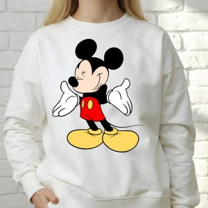 Puede incluir: Sudadera blanca con un dise&ntilde;o de Mickey Mouse sonriendo. El personaje de dibujos animados se representa con orejas negras, camisa roja, zapatos amarillos y guantes blancos. Es una prenda informal de manga larga.
