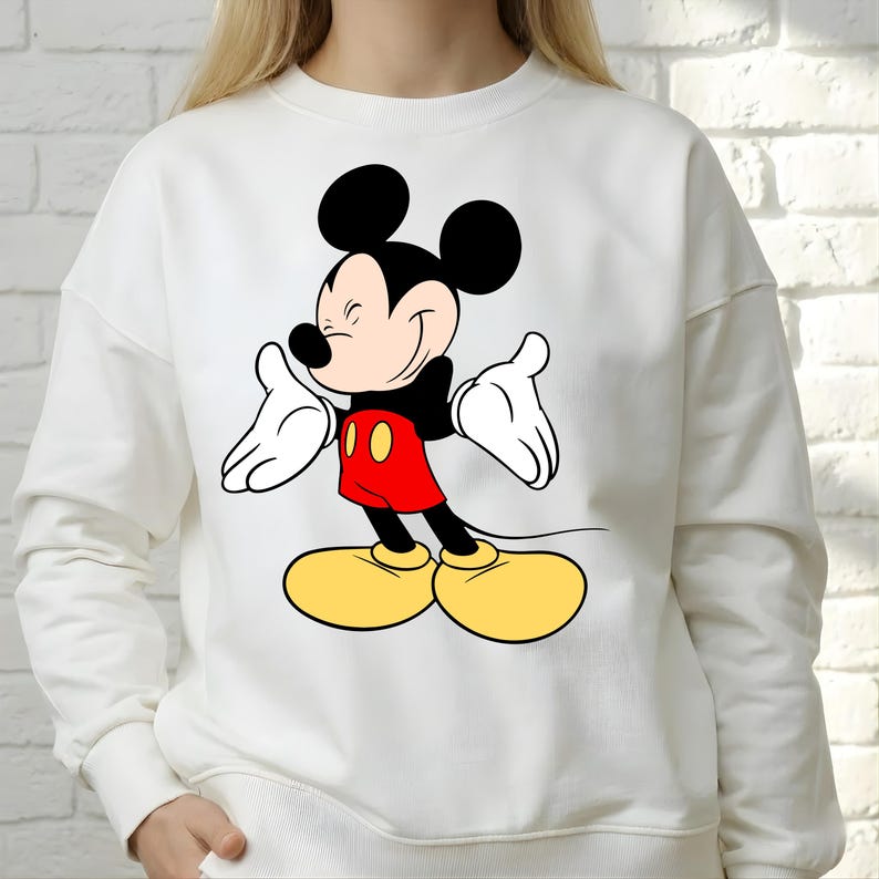 Puede incluir: Sudadera blanca con un dise&ntilde;o de Mickey Mouse sonriendo. El personaje de dibujos animados se representa con orejas negras, camisa roja, zapatos amarillos y guantes blancos. Es una prenda informal de manga larga.