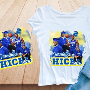 May include: White v-neck t-shirt featuring a graphic design with multiple images of a person in a graduation cap and basketball uniform. The design includes the name "Jermaine Hicks" in blue and yellow text. A pair of blue jeans is visible.