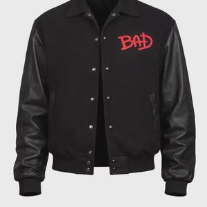 May include: Black varsity jacket with red "BAD" text on the chest. The jacket features black leather sleeves, a button-up front, and a classic collar. A stylish outerwear piece.