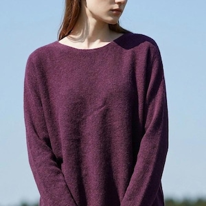 May include: A long-sleeved, deep purple jumper featuring a wide, rounded neckline and a textured knit fabric. The garment has a relaxed fit with straight sleeves and a simple, unadorned hemline, providing a clean and straightforward appearance.