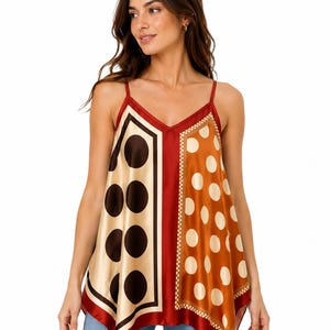May include: A sleeveless camisole top featuring a V-neckline and thin spaghetti straps. The garment is constructed from a satin-like fabric with a split-panel design, showcasing large dark brown polka dots on cream and light tan polka dots on rust.