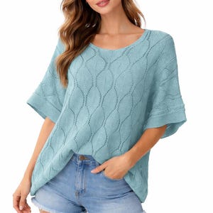 May include: A light blue short-sleeved knit sweater featuring a repeating leaf-like openwork pattern throughout the fabric, a wide round neckline, and loose-fitting sleeves, paired with light blue denim shorts with a frayed hemline.