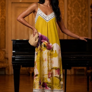Peut inclure: Une robe midi jaune moutarde avec de fines bretelles et un décolleté en V. La robe présente une bordure blanche avec du texte cursif noir, un imprimé floral artistique dans des tons violets et verts, et un ourlet blanc avec du texte noir.