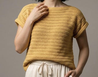 May include: Mustard yellow crochet top with short sleeves and a boat neck. The top is paired with off-white drawstring pants. The crochet stitch creates a textured, horizontal striped pattern. The sleeves are cuffed. The overall style is casual and comfortable.