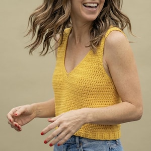Puede incluir: Un top de crochet amarillo con cuello en V. El top sin mangas está hecho de una tela texturizada de tejido abierto. El top es de color amarillo brillante y soleado.
